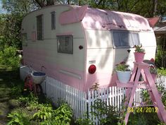 an old pink and white trailer parked next to a fence with potted plants on it