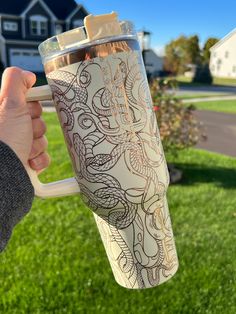 a person holding a coffee cup in their hand on the grass with houses in the background