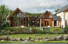 a house with lots of windows sitting next to a lush green field and rock garden