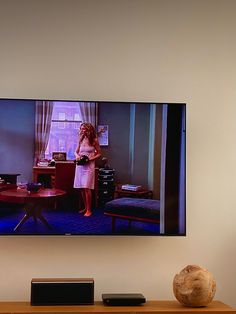 a woman standing in front of a flat screen tv on a wall above a wooden table