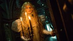 a woman with long blonde hair holding two candles in front of her face and looking at the camera