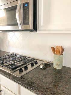 a stove top oven sitting inside of a kitchen next to a microwave and wooden utensils