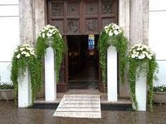 an entrance to a building with white flowers and greenery on the columns, along with potted plants