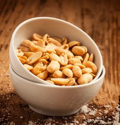 two white bowls filled with nuts on top of a wooden table