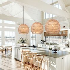 an open kitchen with wooden chairs and hanging lights above the island counter, in front of large windows