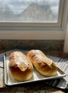 two loaves of bread sit on a plate next to a window