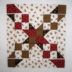 a close up of a quilted wall hanging on a white wall with red and brown designs