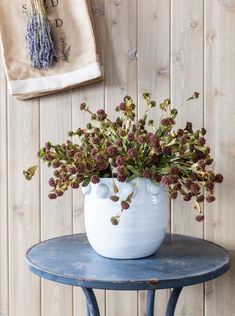 a white vase filled with purple flowers sitting on top of a blue table next to a wall