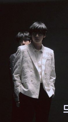 two young men standing next to each other in front of a black background, one wearing a white jacket