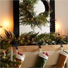 christmas stockings hanging from the mantle in front of a mirror with candles and wreaths