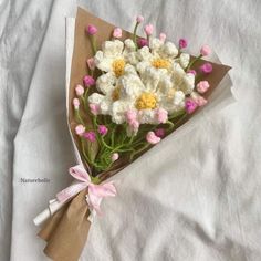 a bouquet of white and pink flowers wrapped in brown paper on top of a bed