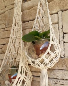 two macrame plant holders with plants in them hanging on a wall next to a stone wall