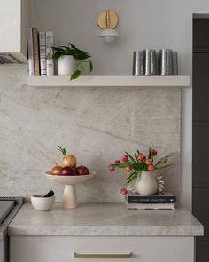 a kitchen counter with flowers, fruit and books on the shelf above it is a vase filled with tulips