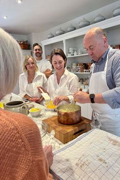 a group of people standing around a kitchen preparing food on top of a wooden cutting board