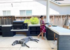 a woman standing next to a grill with a dog laying on the ground