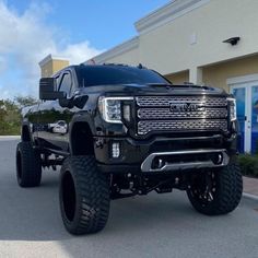 a black truck is parked in front of a building with large tires on it's sides