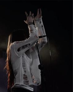 a woman with long hair holding her hands up in the air while standing next to a microphone