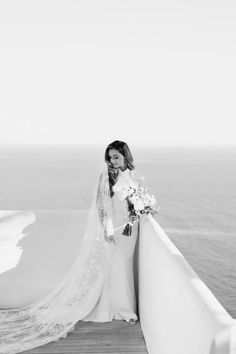 a woman standing on top of a pier next to the ocean wearing a wedding dress