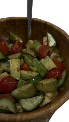 a wooden bowl filled with cucumbers, tomatoes and other vegtables