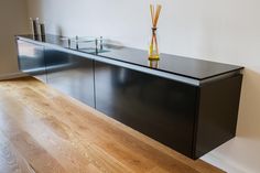 a black cabinet with two vases on top of it next to a wooden floor