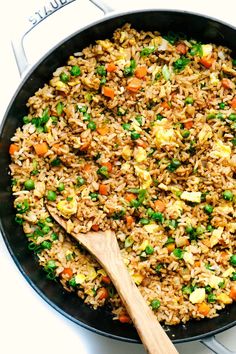 a skillet filled with rice and vegetables next to a wooden spoon on top of a stove