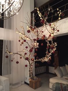 a christmas tree decorated with ornaments and lights in a living room next to a window