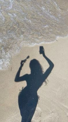 a shadow of a woman holding a cell phone on the beach