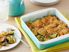 a casserole dish with broccoli and cheese on the side next to a glass of water