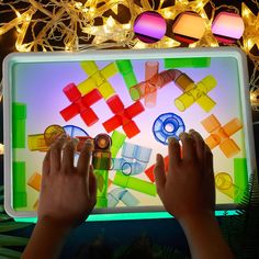 two hands are playing with an interactive game on a tablet screen at night time, surrounded by lights and garlands