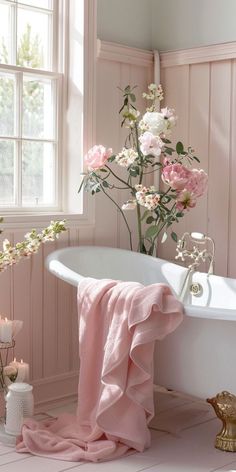 a white bath tub sitting next to a window with pink flowers in it and candles on the floor