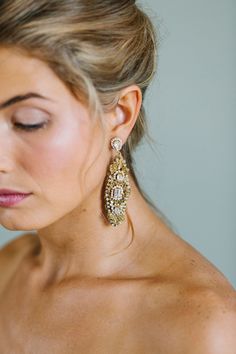 a woman wearing large gold earrings on her shoulder and looking down at the camera with eyes closed