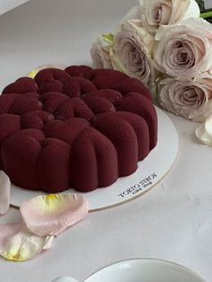 a red velvet cake on a white plate with flowers in the background and a bouquet of pink roses