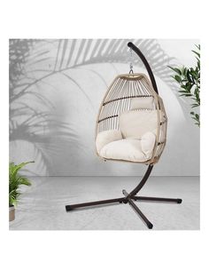 a hanging chair with a white cushion on it and a plant in the corner next to it