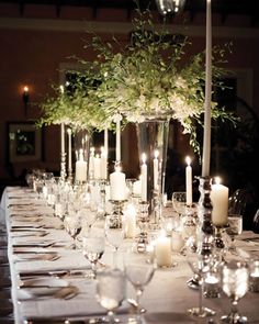 an image of a table setting with candles and greenery in vases on it