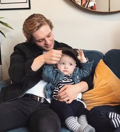 a woman combs her baby's hair while sitting on a couch