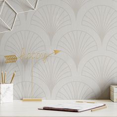 a desk with a notebook, pen and pencil holder on it next to a wallpapered background