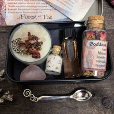 an assortment of items in a tray with spoons and bottles next to it on a table