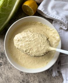 a white bowl filled with soup next to lettuce and lemons on a table