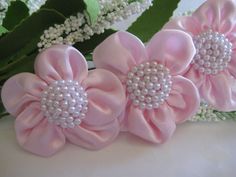 three pink flowers with pearls on them sitting next to some green leaves and white flowers