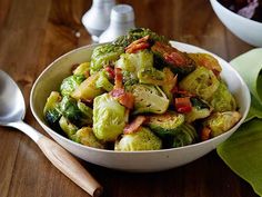 a white bowl filled with brussel sprouts and bacon on top of a wooden table