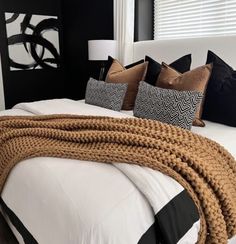 a white bed topped with lots of pillows next to a black and white headboard