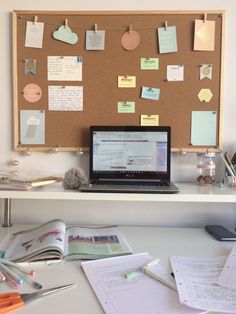 a laptop computer sitting on top of a desk covered in notes and memos next to a cork board