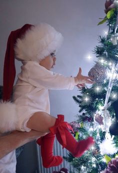 a baby wearing a santa hat and sitting in front of a christmas tree with lights