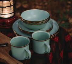 a table topped with plates and cups on top of a wooden cutting board next to a lantern