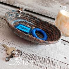 a basket with a keychain attached to it sitting on a wooden table next to a candle