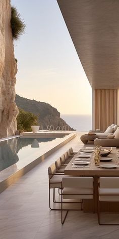 an outdoor dining area with table and chairs next to the pool overlooking the ocean at sunset