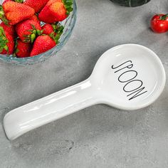 a bowl of strawberries next to a spoon with the word woom on it