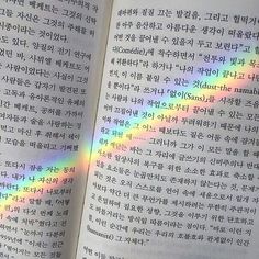 an open book with rainbow colored text on the pages and in english writing, there is a bright light coming from behind it