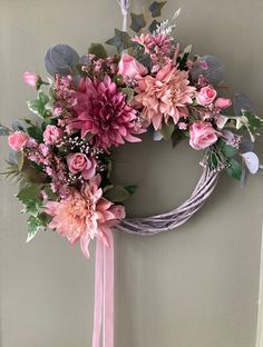 a wreath with pink flowers and greenery hanging on a door handle in front of a gray wall