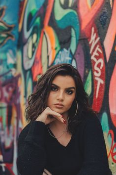 a woman sitting in front of a wall with graffiti on it and her hand under her chin